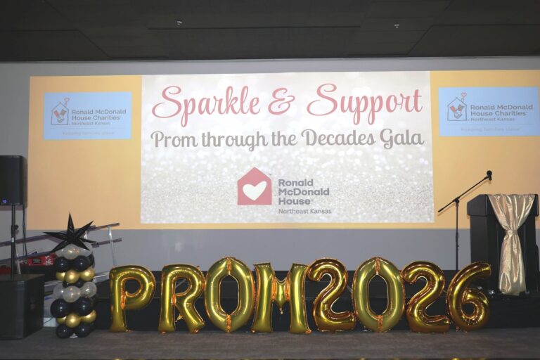 Stage setup for the RMHC Northeast Kansas Sparkle and Support Prom Through the Decades Gala, featuring a projection screen and large gold PROM 2026 balloon letters.